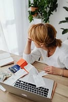 Messy desk with receipts and bills next to laptop showing bank statements