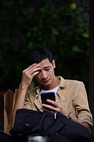 Man stressed while checking his phone after discovering unknown subscription charges draining his bank account