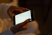 Phone screen showing banking app with positive balance glowing in dark bedroom