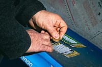 Hand holding scratch off lottery ticket next to pile of losing tickets