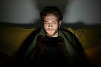 Person sitting on couch in dim lighting looking at phone with honest expression