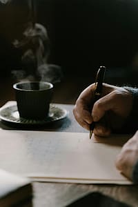 Person writing in notebook with coffee feeling calm and focused on tracking spending