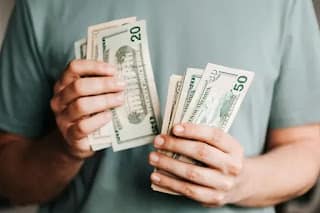 Person counting saved dollar bills on a table showing progress after completing a no spend challenge
