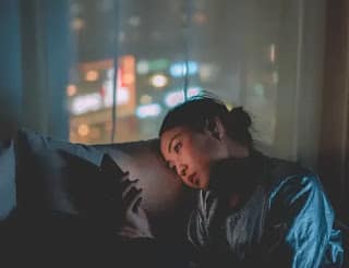 person lying in bed scrolling phone at night thinking about money